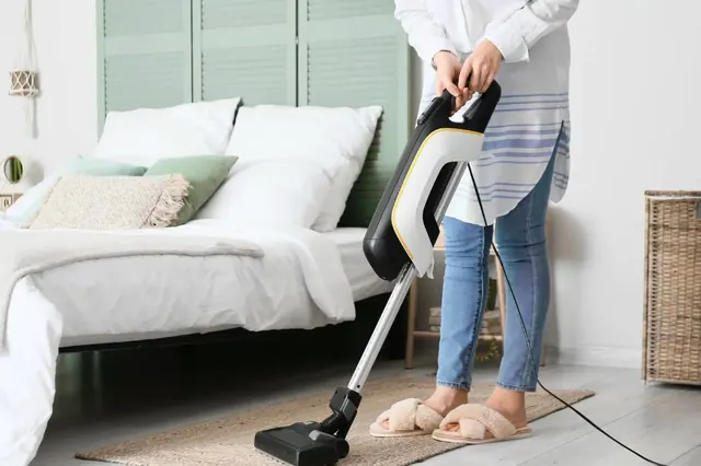 Vacuuming the floor beside a freshly made bed