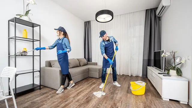 Two Prime Pure cleaners dusting shelves and mopping the floor of a bright living room