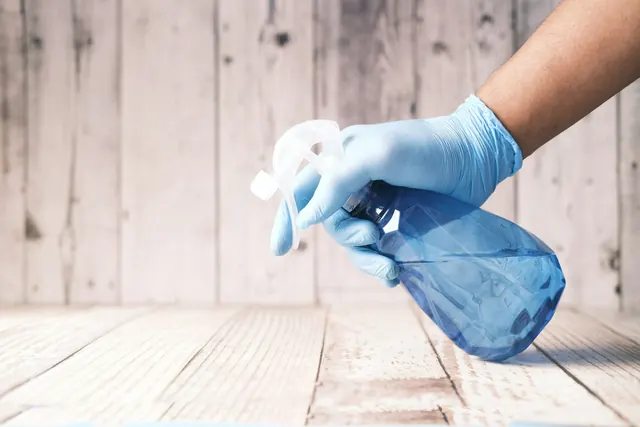 Gloved hand spraying cleaner onto a surface