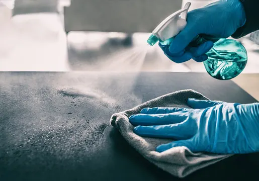 Gloved hands spraying and wiping a surface clean